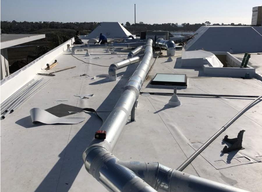 Commercial flat roof replacement in progress with new membrane installation around HVAC ductwork and skylight
