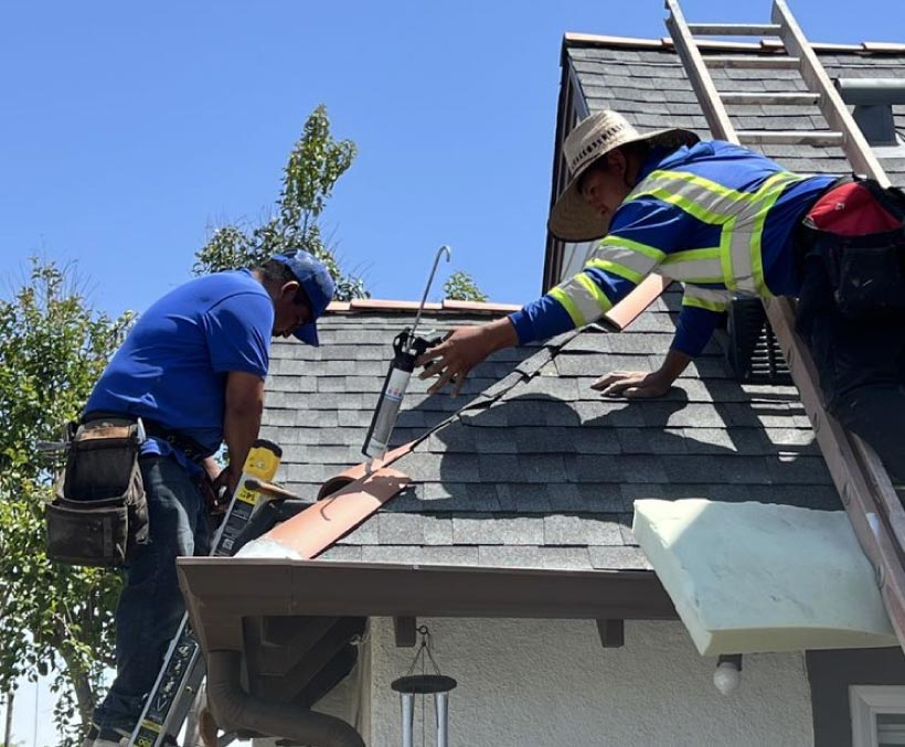 roof-sealant Roofers applying sealant along a shingle roof edge and gutter during a repair