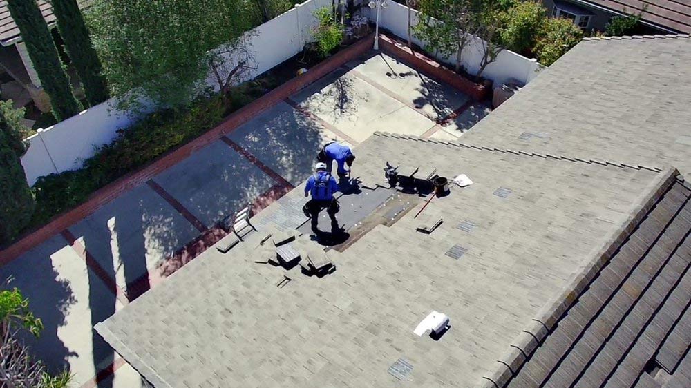 Roofers repairing an asphalt shingle roof section near a pool in Lakewood, CA