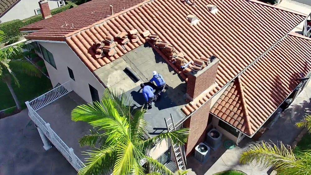 Aerial view of roofers repairing a clay tile roof around a chimney