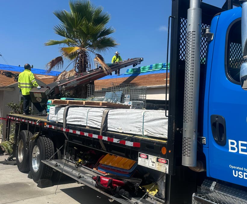 roofing-service Flatbed truck delivering roofing materials to a job site with crew unloading on the roof