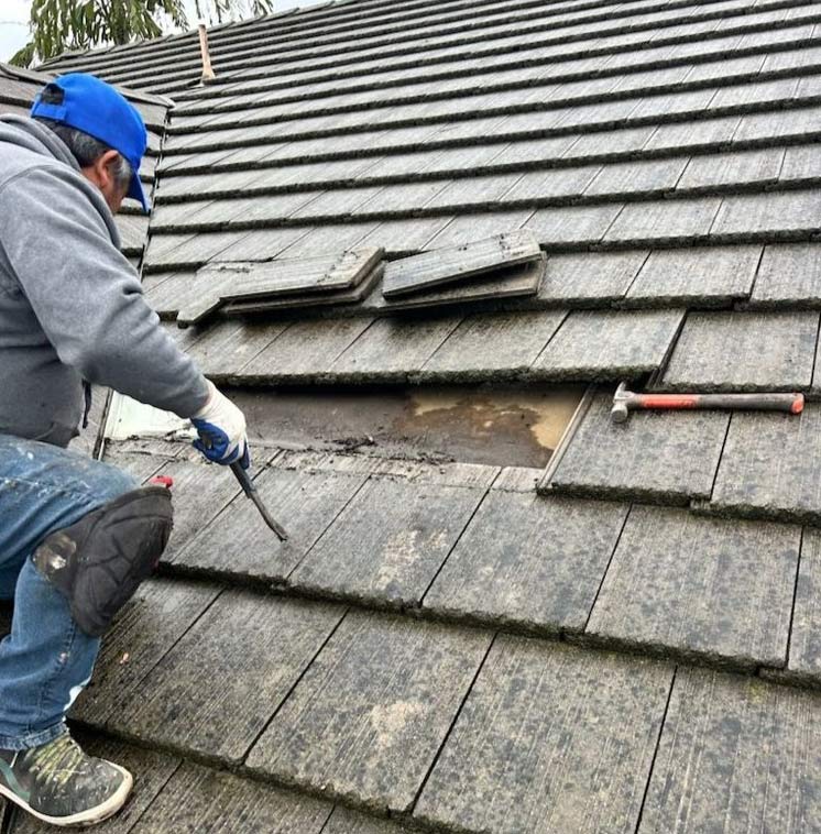 Roofer removing damaged flat concrete tiles to repair a tile roof in Lakewood, California