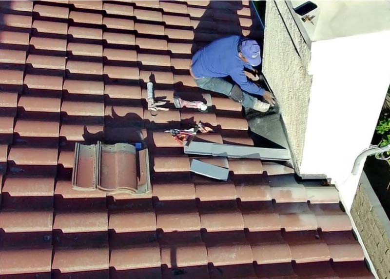 Roofer replacing broken clay roof tiles during a tile roof repair