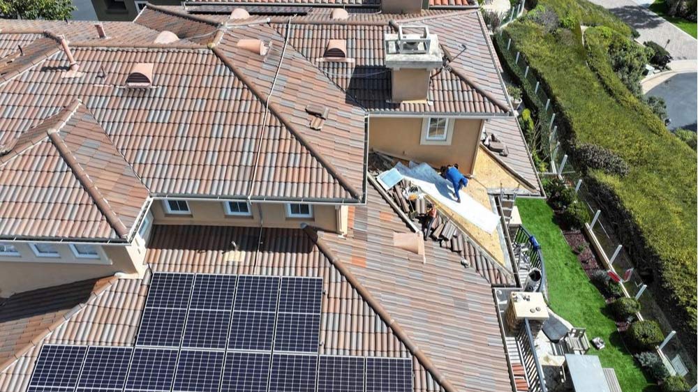 Aerial view of a tile roof repair with underlayment installation in progress, showing solar panels on the same roof